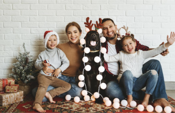 Family with Mom, Dad, son and daughter and dog wearing santa hats and reindeer headbands with Christmas decor around them